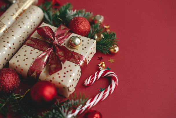 Boldog Karácsonyt és Kellemes Ünnepeket! Modern karácsonyi kompozíció. Stílusos karácsonyi ajándék, csomagolópapír, fenyő ágak, cukornád és baubles piros alapon, másolás helyet. Ünnepi zászló - Fotó, kép