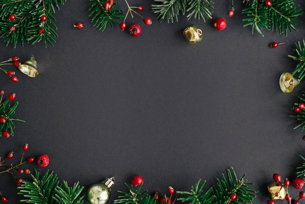 Kerst plat gelegd. Stijlvolle kerstboom takken, rode bessen en gouden kerstballen frame compositie op zwarte achtergrond. Seizoen wenskaart template, ruimte voor tekst. Fijne feestdagen! - Foto, afbeelding