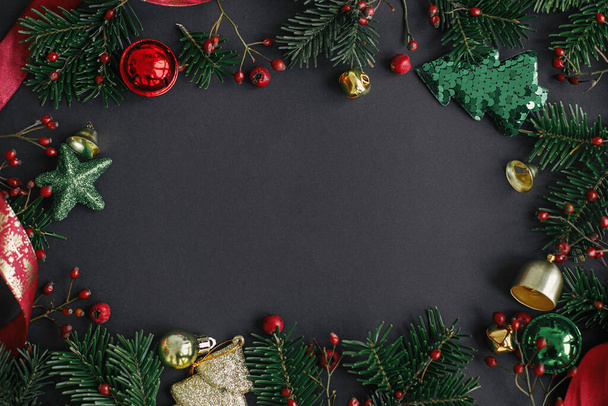 メリークリスマスとハッピーホリデー!スタイリッシュなクリスマスツリーの枝、赤い果実と金の装飾品のフレームフラットブラックの背景に横たわります。シーズンのグリーティングカードテンプレートテキストのスペース - 写真・画像
