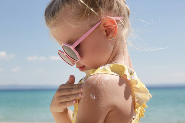 Roztomilé malé 4 letá dívka aplikující krém na ochranu proti slunečnímu záření na pláži. Krém proti slunci na ochranu dítěte před sluncem během letních prázdnin. Děti péče o pleť během cesty. - Fotografie, Obrázek