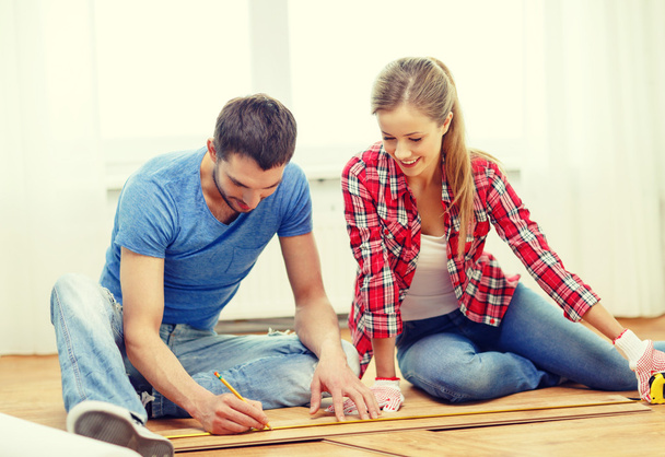 smiling couple measuring wood flooring - Foto, afbeelding