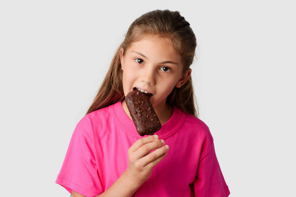 Beautiful girl in a pink T-shirt eating chocolate ice cream with nuts. Small child happy to get tasty ice cream in a hot Summer day - Fotografie, Obrázek