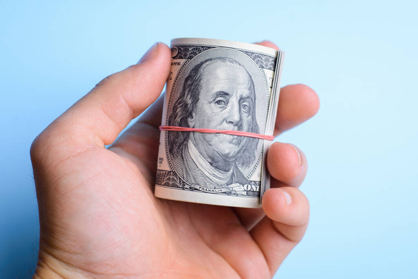 Hand holding a wad of dollars cash over a blue background - Photo, Image