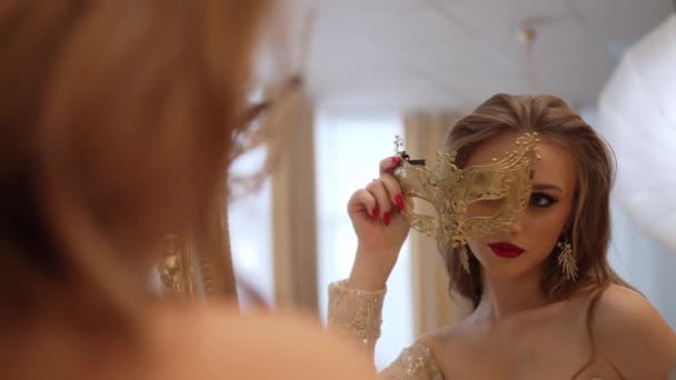 Красивая девушка в роскошном платье покрывает лицо маскарадной маской - Кадры, видео