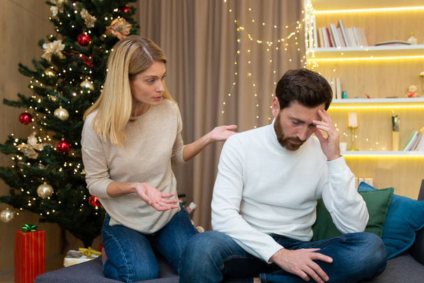 Family quarrel on Christmas New Year holiday, woman shouts and quarrels on husband, couple at home sitting on sofa near Christmas tree. - Foto, immagini