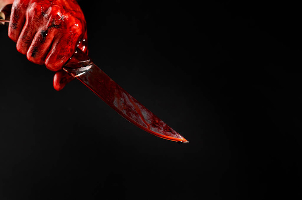 A man with bloody hands brandishes a knife on a black background - Fotó, kép