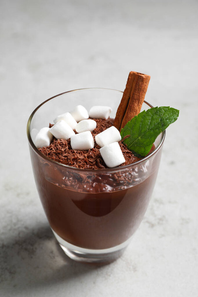 Μια κούπα νόστιμη ζεστή σοκολάτα με ζαχαρωτά, ξυλάκι κανέλας και μέντα σε ανοιχτό γκρι τραπέζι - Φωτογραφία, εικόνα