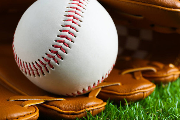Catcher's mitt and baseball ball on green grass, closeup. Sports game - 写真・画像