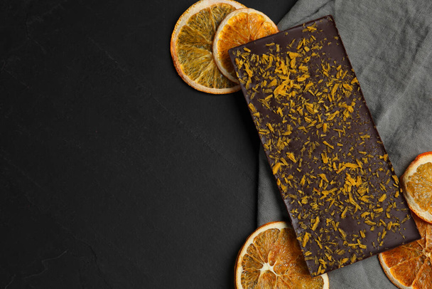Chocolate bar with freeze dried orange on black table, flat lay. Space for text - Foto, Bild