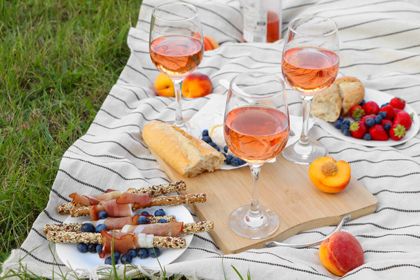 Glasses of delicious rose wine and food on picnic blanket outdoors - Φωτογραφία, εικόνα