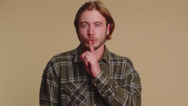 Csendet kérek. Portré szakállas felnőtt férfi 20 éves prések mutatóujj az ajkak teszi csend gesztus jel nem árulja el a titkot. Fiatal felnőtt jóképű srác pózol bézs stúdió háttér - Felvétel, videó