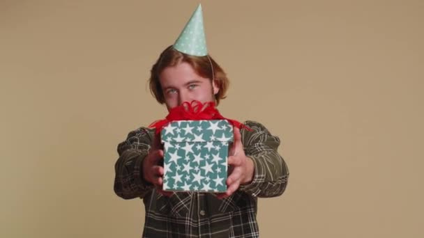 Positiv lächelnder bärtiger Mann präsentiert Geburtstagsgeschenkbox streckt Hände aus, überreicht verpacktes Geschenk Karrierebonus, feiert Party. Junge erwachsene Kerl Junge isoliert allein auf beige Studio Wand Hintergrund - Filmmaterial, Video