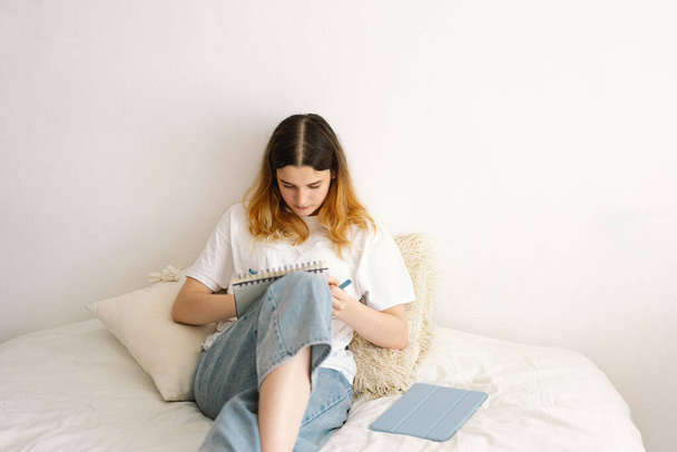 Ein Mädchen im Teenageralter zeichnet oder macht Hausaufgaben im Schlafzimmer. Ein Teenager lernt zu Hause. Zurück zur Schule - Foto, Bild