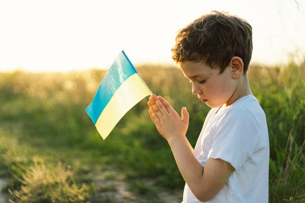 Ukrán fiú becsukta a szemét, és imádkozik, hogy állítsa le a háborút Ukrajnában egy mezőn naplementekor. A hit, a spiritualitás és a vallás imáiban összehajtogatott kezek. Oroszország háborúja Ukrajna ellen. Hagyd abba! - Fotó, kép
