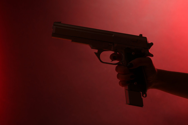 Hand holding gun on red background - Foto, Imagen