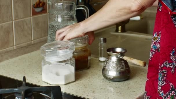 Μια νοικοκυρά βάζει ζάχαρη σε μια Τουρκική καφετιέρα με ένα κουταλάκι του γλυκού, ο καφές προσθέτει λίγο αλάτι από ένα αλατωρυχείο και ρίχνει νερό από μια καράφα, ανάβει μια σόμπα αερίου και βάζει φωτιά στον Τούρκο. Κοντινό πλάνο. - Πλάνα, βίντεο