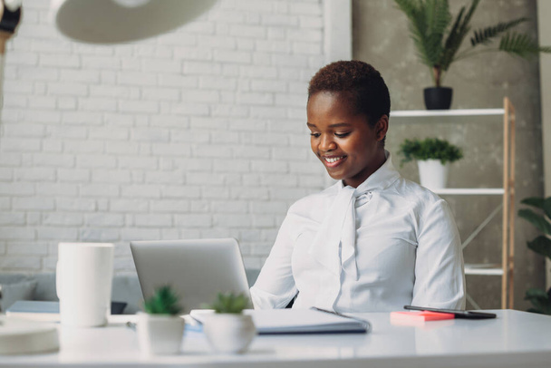 Зосереджена молода афроамериканська бізнесменка, яка дивиться на екран ноутбука, друкує на клавіатурі комп'ютера в сучасному офісі корпорації. Комунікаційна мережа - Фото, зображення