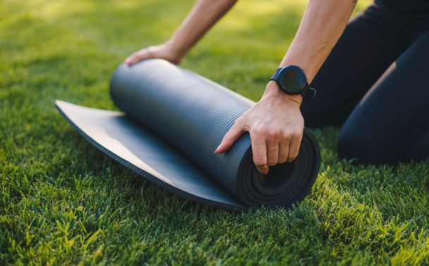 Een zwarte yoga mat uitrollen voor een yoga les in het park. Sluit het beeld. Gezonde levensstijl, sport. Gezonde activiteit. Mensen levensstijl concept. Opleiding - Foto, afbeelding
