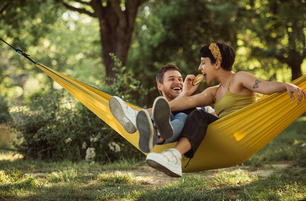 Pretty couple relaxing on a yellow hammock while the boy is feeding his girlfriend with a sandwich - Photo, Image