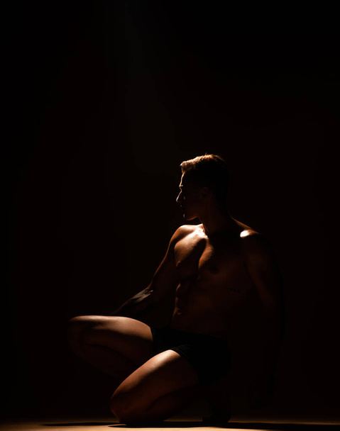 Silhouette of a handsome man standing on his knee at the studio - Foto, afbeelding