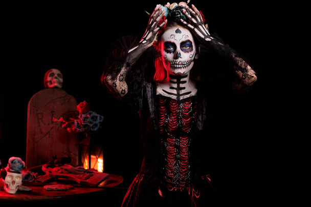 Ιερά θεά του θανάτου αγγίζοντας το στεφάνι των τριαντάφυλλων για να γιορτάσει το μεξικάνικο dios de los muertos στο στούντιο, που μοιάζει με la cavalera catrina. Γυναίκα με ασπρόμαυρο σώμα τέχνης, αποκριές πολιτισμού. - Φωτογραφία, εικόνα