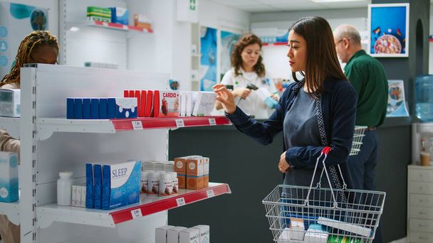 Asiatische Kunden betrachten Medikamentenboxen und Tablettenflaschen in den Regalen, checken Arzneimittel, um medizinische Produkte und Nahrungsergänzungsmittel zu kaufen. Frau liest Beipackzettel für Medikamente. - Foto, Bild