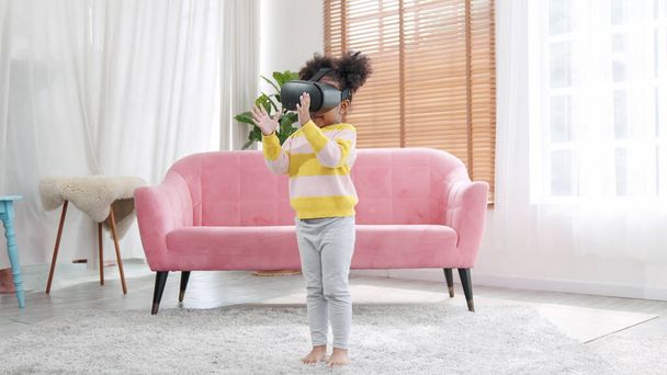 Retrato de disfrutar de los niños felices utilizando la tecnología de juego metaverso VR en la sala de estar en casa. Niño sonriendo y divirtiéndose usando gafas de realidad virtual tecnología de auriculares jugando deporte - Foto, imagen