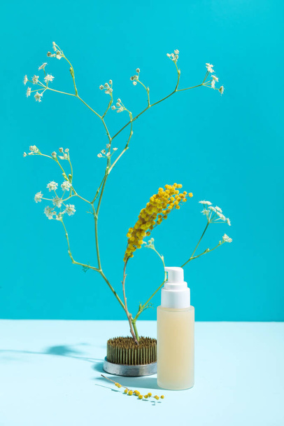 Bottle of cosmetic product with ikebana on blue background - Фото, изображение