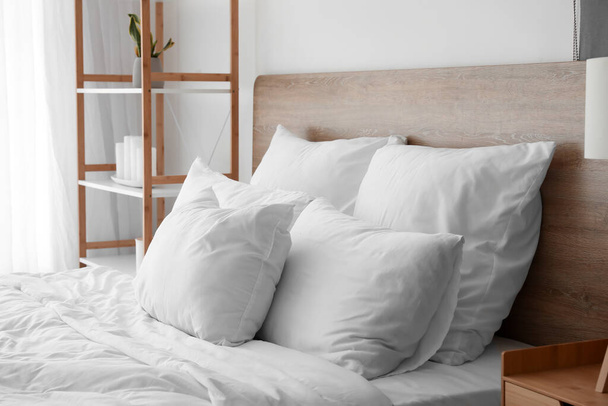 Groot bed met zachte kussens in lichte slaapkamer - Foto, afbeelding