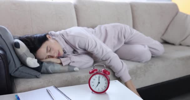A nő a kanapén fekszik, párnával takarja a fejét, és csörög az ébresztőóra. Fáradtság és álmosság fogalma - Felvétel, videó