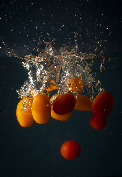 Cherry tomatoes falling in water causing splashes. Concept of freshness and good health through nutrition - Фото, изображение