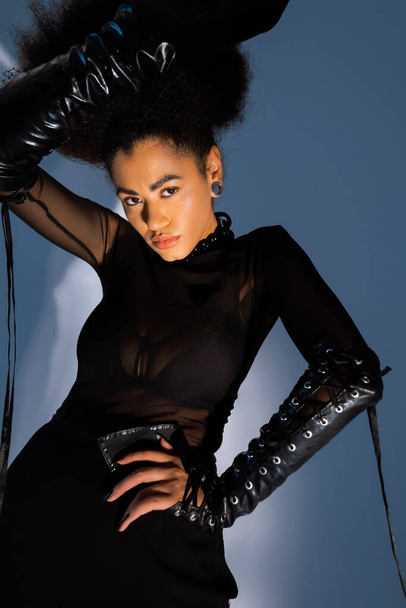 trendi afro-amerikai modell fekete ruhában pózol kéz a csípőn kék  - Fotó, kép