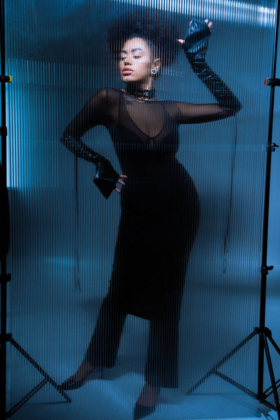full length of young african american model in sexy black outfit posing behind ruffled glass - Photo, image