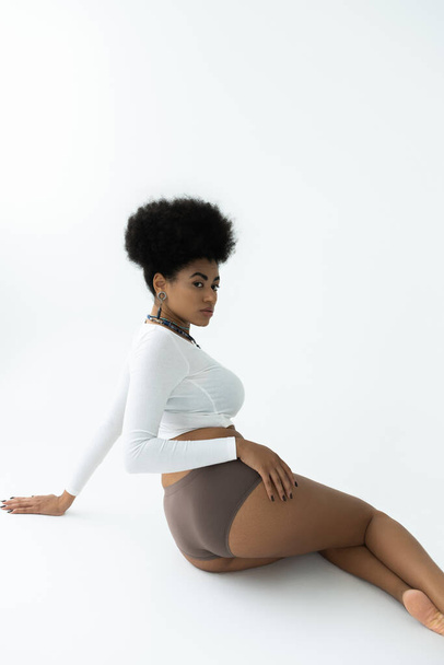 young african american woman posing in long sleeve shirt and panties while sitting on white  - Foto, immagini