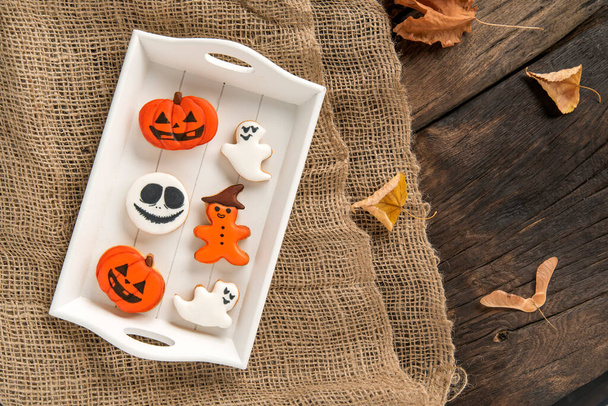 Halloween sweets lie in a wooden tray. Orange gingerbread in pumpkin shape and ghosts. Tasty cookie on table. Top view. - Photo, Image