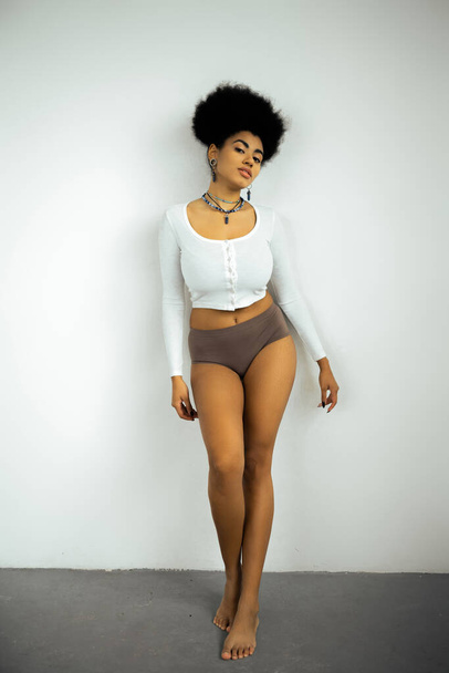 full length of barefoot african american woman in long sleeve shirt and panties standing near white wall  - Φωτογραφία, εικόνα