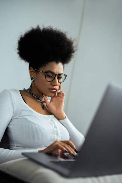 concentrated african american woman in eyeglasses using laptop at home - Foto, afbeelding