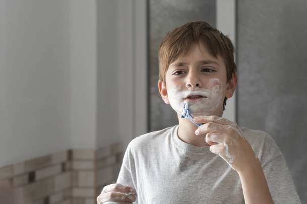 Oğlan, babası gibi sakalını tıraş köpüğüyle taklit ediyor. Oğlan banyoda eğlencelidir. - Fotoğraf, Görsel