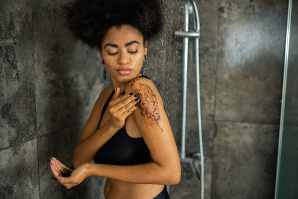Curly mulher americana africana na colheita top massageando ombro com esfrega de café no chuveiro  - Foto, Imagem