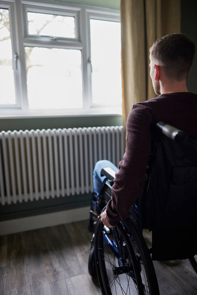 Rear View Of Depressed Man With Poor Mental Health In Wheelchair By Window At Home - Foto, Imagem