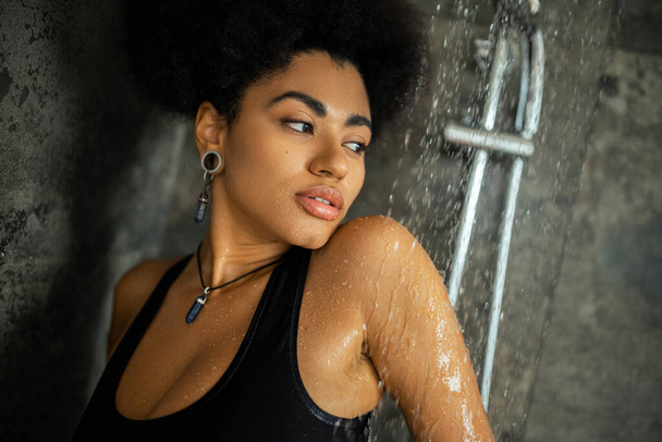 Young curly african american woman in crop top looking away while taking shower  - Foto, Imagen