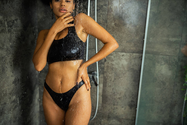 Cropped view of african american woman in crop top and panties taking shower and looking at camera at home  - Foto, Imagen