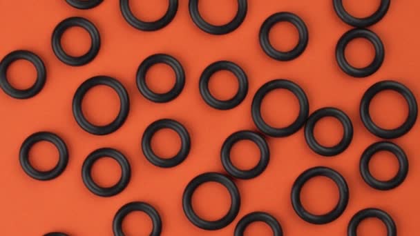 Abstract bovenaanzicht van zwarte ronde rubberen pakkingen op een kleurrijke oranje achtergrond. Geometrische vormen details close-up. Rotatie - Video