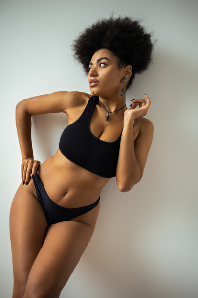 Sexy african american woman in crop top and panties touching hip while standing near wall  - Фото, изображение