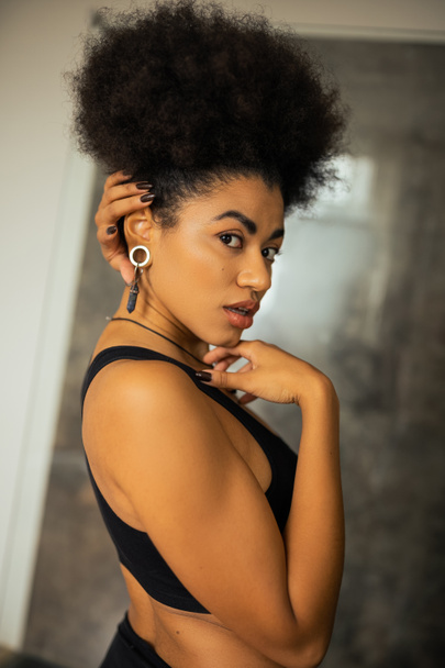 Portrait of young african american woman in crop top looking at camera in blurred bathroom  - Photo, Image