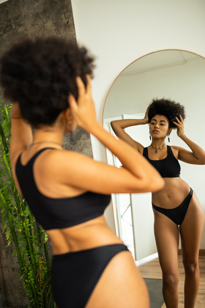 Back view of african american woman in underwear touching hair while standing near mirror in bathroom  - Φωτογραφία, εικόνα