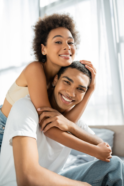 frisée afro-américaine femme embrassant petit ami heureux et regardant caméra - Photo, image