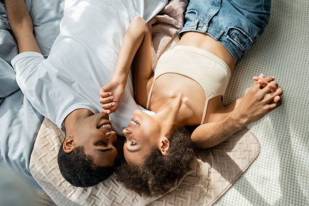 top view of sexy african american woman touching chin of boyfriend while lying on bed - Foto, Imagem