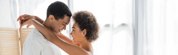 vue de côté de femme afro-américaine heureuse embrassant petit ami heureux à la maison, bannière - Photo, image