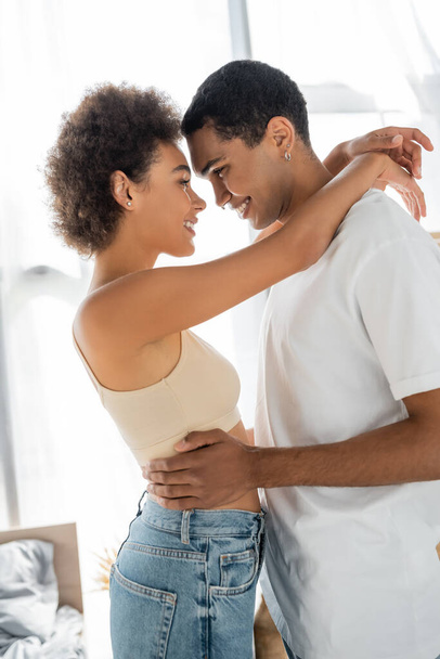 side view of african american couple embracing and smiling while standing face to face - Photo, Image